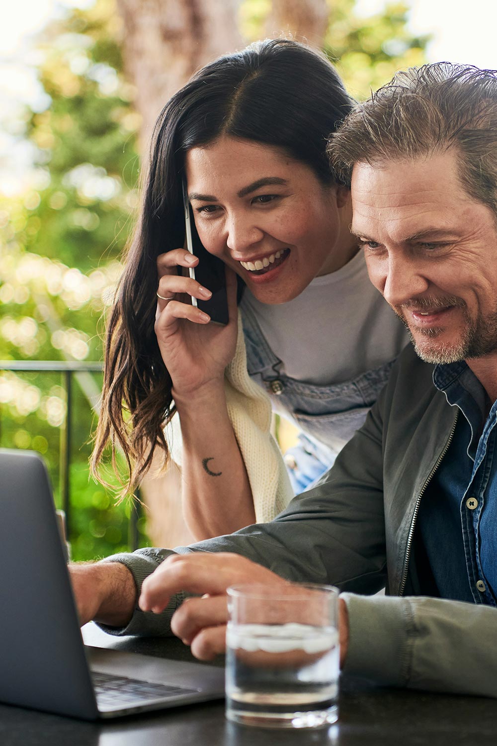 Man using her computer and a woman talking on the phone beside the man
