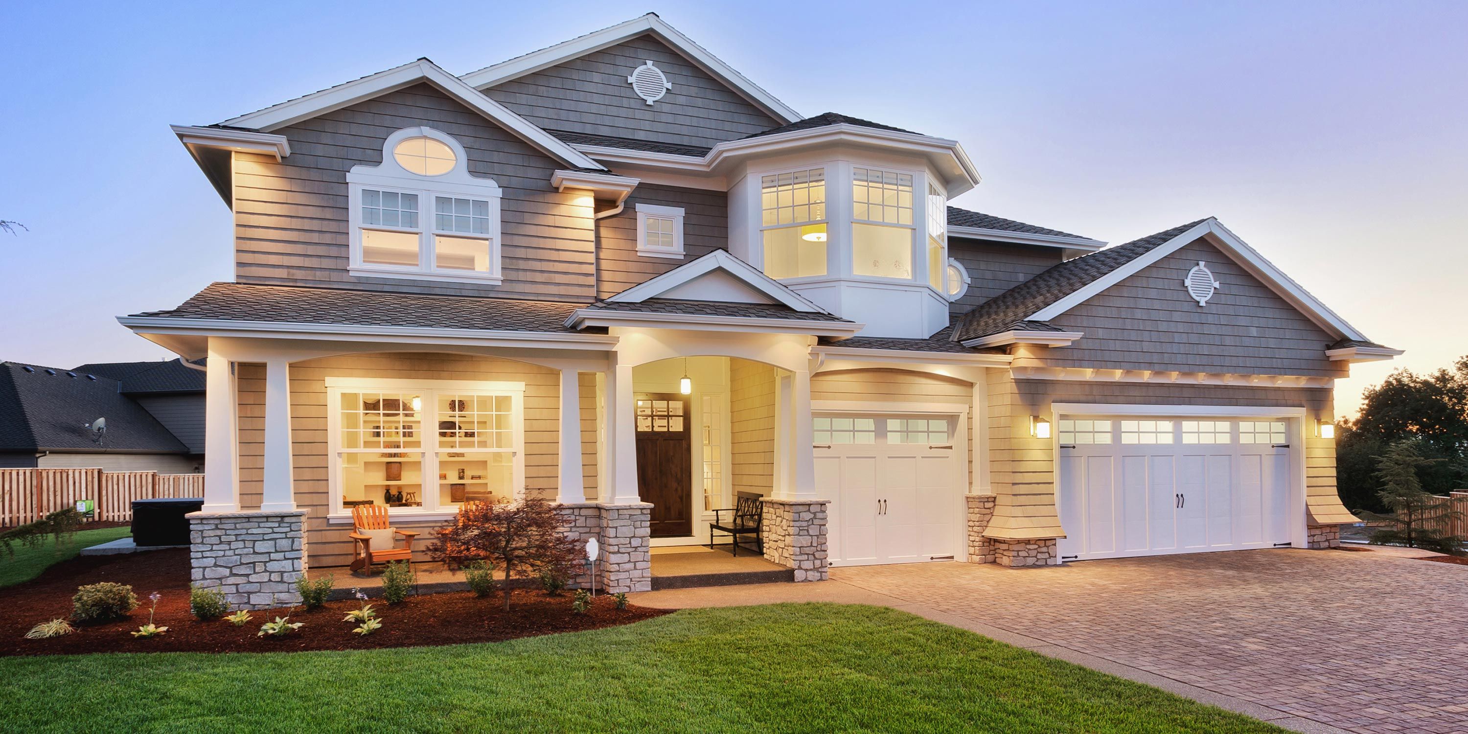 Modern two-story house with warm exterior lighting, featuring a welcoming front porch and well-kept lawn.