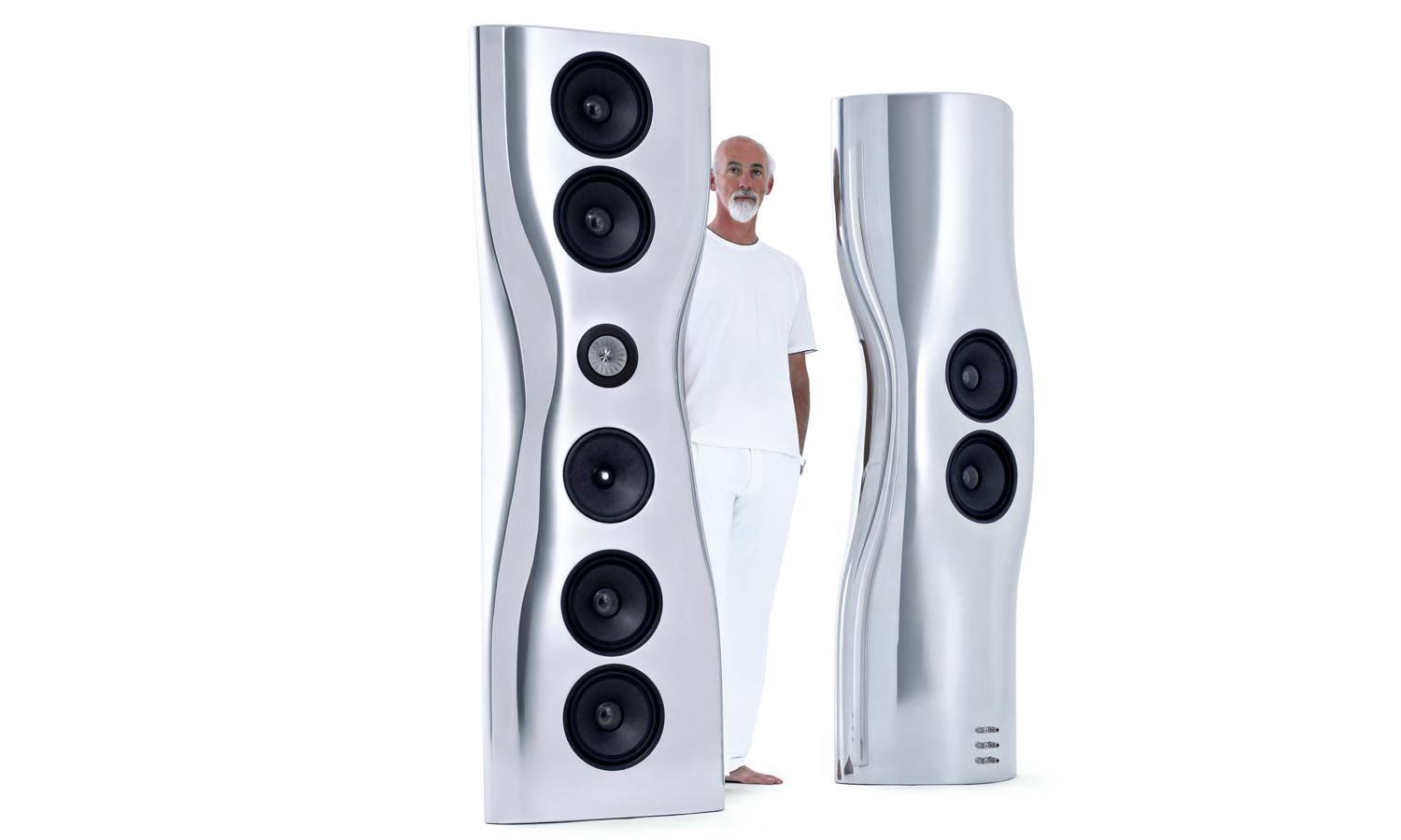 A man standing next to a pair of futuristic silver KEF Muon speakers against a white background.