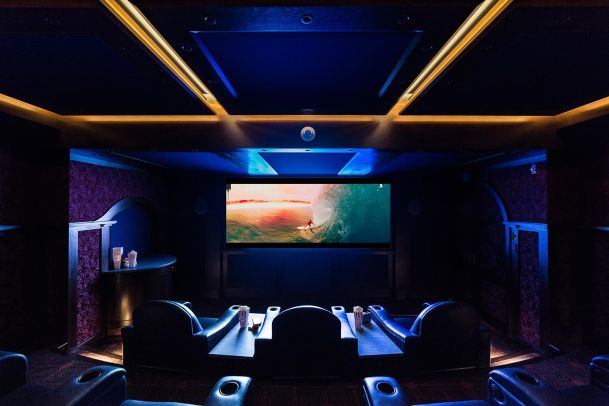 Luxurious home theater with leather recliners, ambient lighting, and a large screen displaying a surfer.