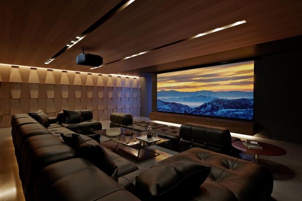 A luxurious home theater with dark leather seating, a large screen showing a mountain sunset, and wooden paneling.