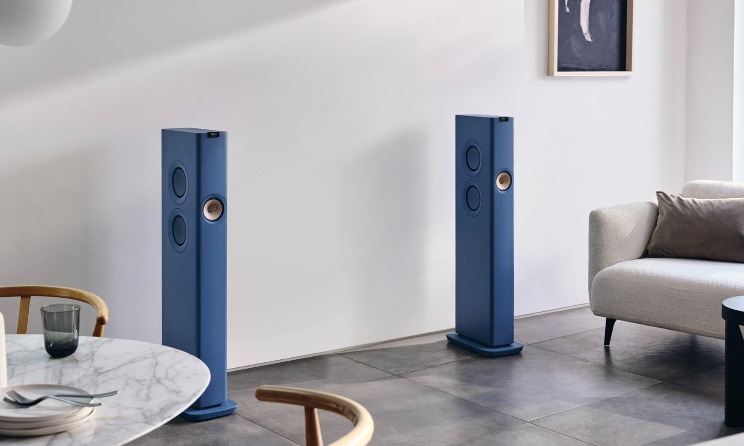 A pair of blue KEF LS60 Wireless speakers in a modern living room with minimalist decor.