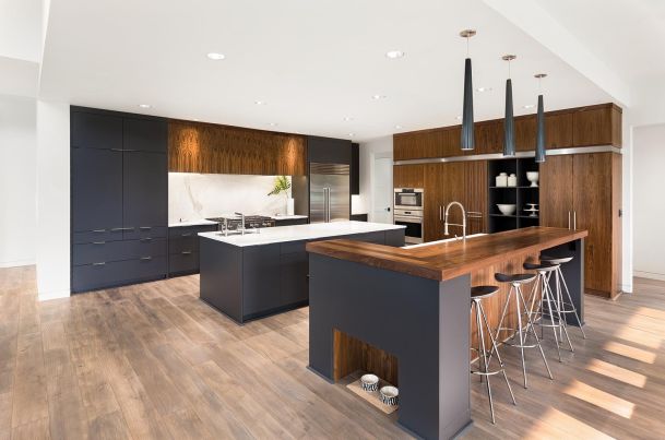 A modern kitchen with dark cabinetry, a large wooden island with seating, and stainless steel appliances, featuring a combination of wood and marble elements.