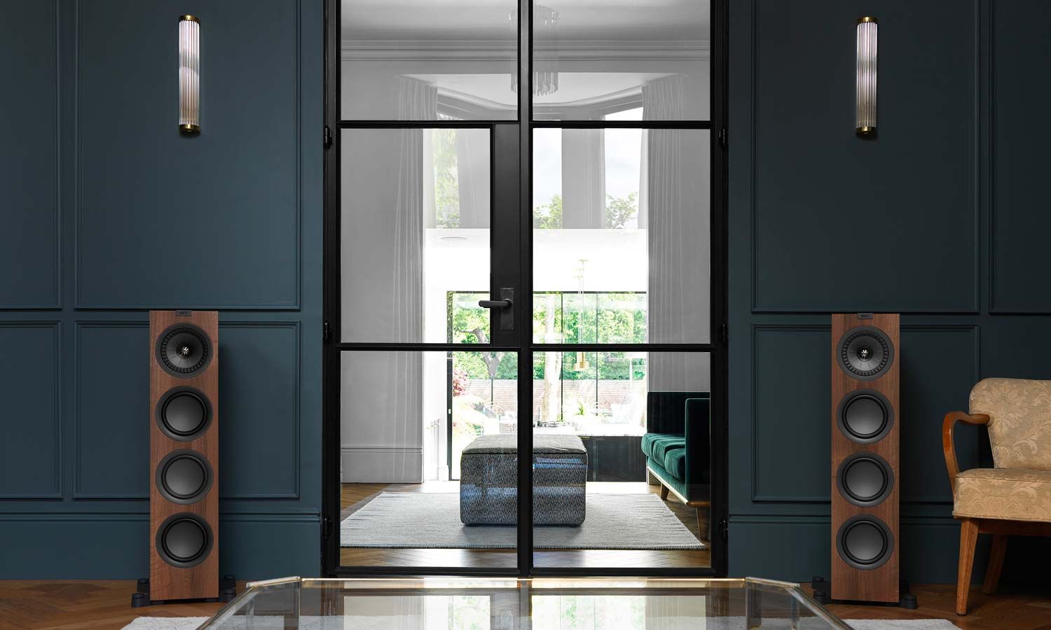 A pair of KEF Q Series floor-standing speakers in a stylish living room with dark blue walls and a glass door.