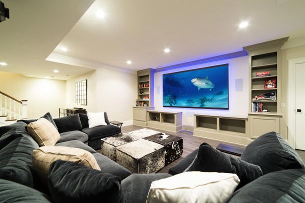 Spacious home theater with a large sectional sofa, a big screen, and shelves with decor.