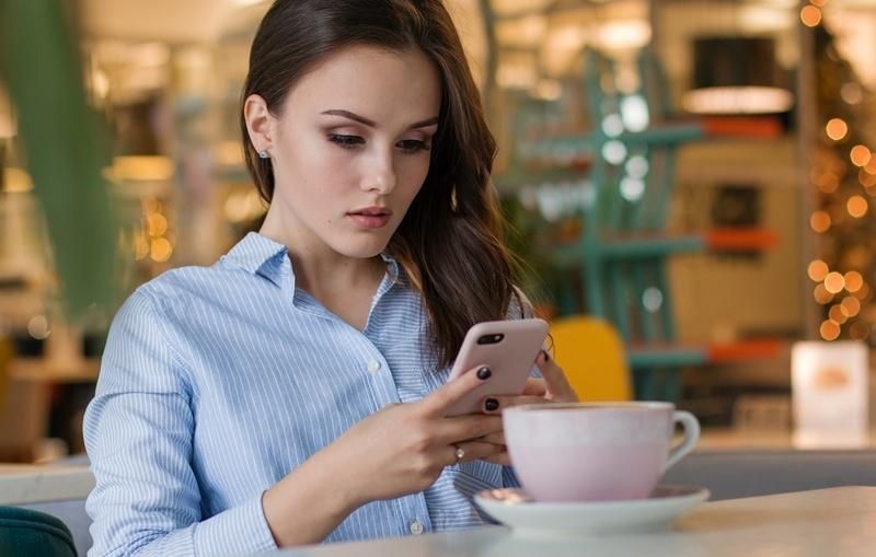 Woman using a smartphone in a cafe, likely interacting with Hunter Douglas PowerView.