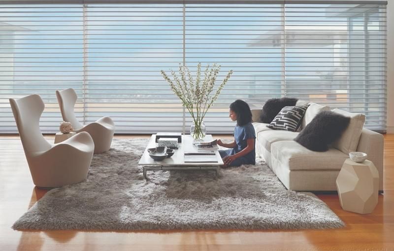 Woman sitting in a modern living room with Hunter Douglas PowerView motorized shades in the background.