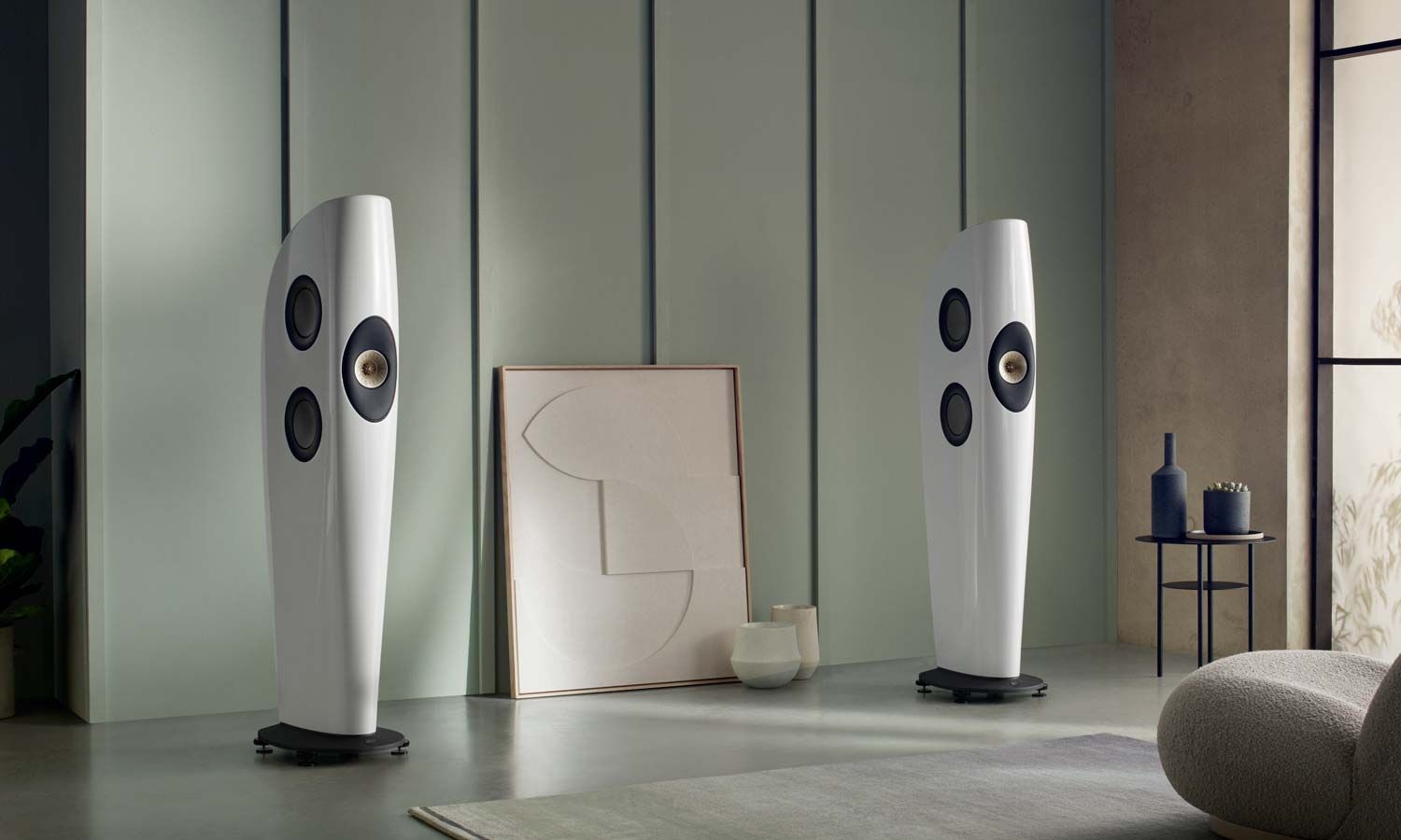 A pair of white KEF Blade Series speakers displayed in a minimalist living room with modern decor.