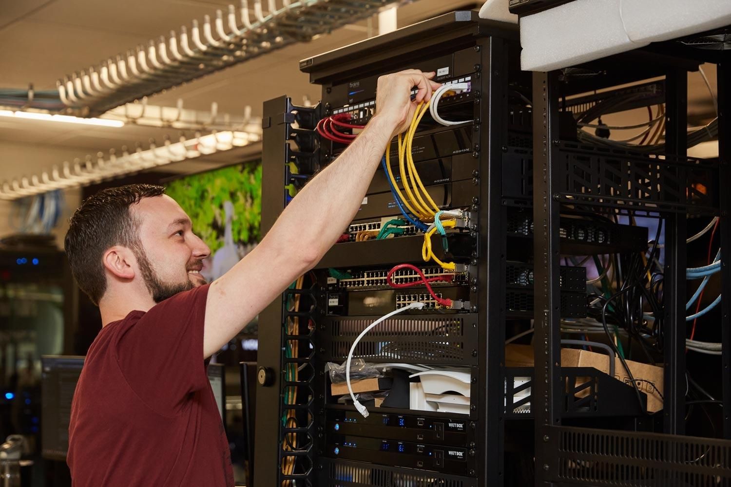 Technician organizing and connecting wires in a server rack in a technology room.