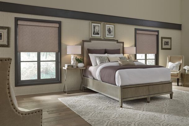 A serene bedroom with a light-colored bed, soft gray accents, and two windows with beige shades, flanked by nightstands and table lamps.