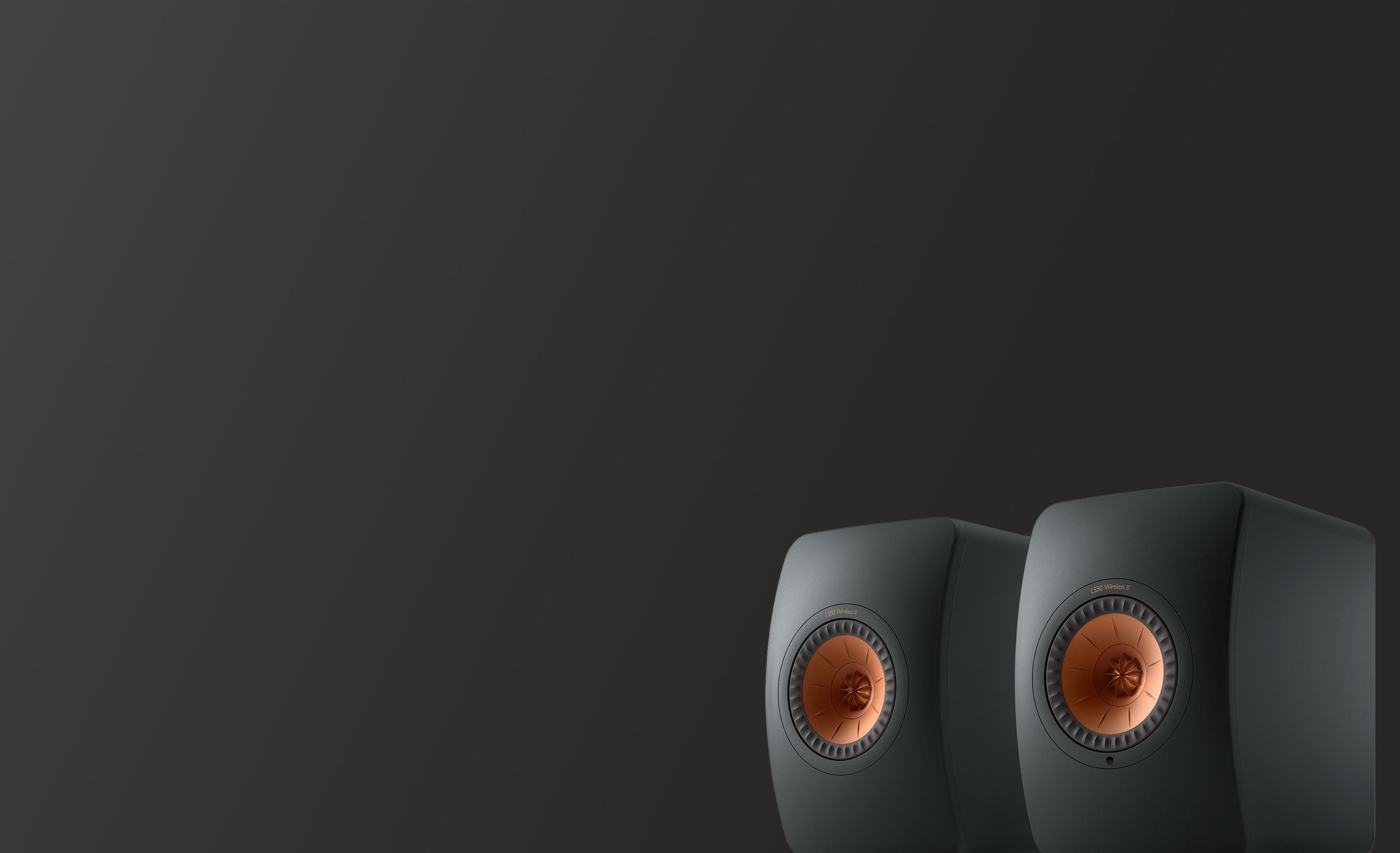 A pair of black KEF LS50 Wireless speakers with copper drivers against a dark background.