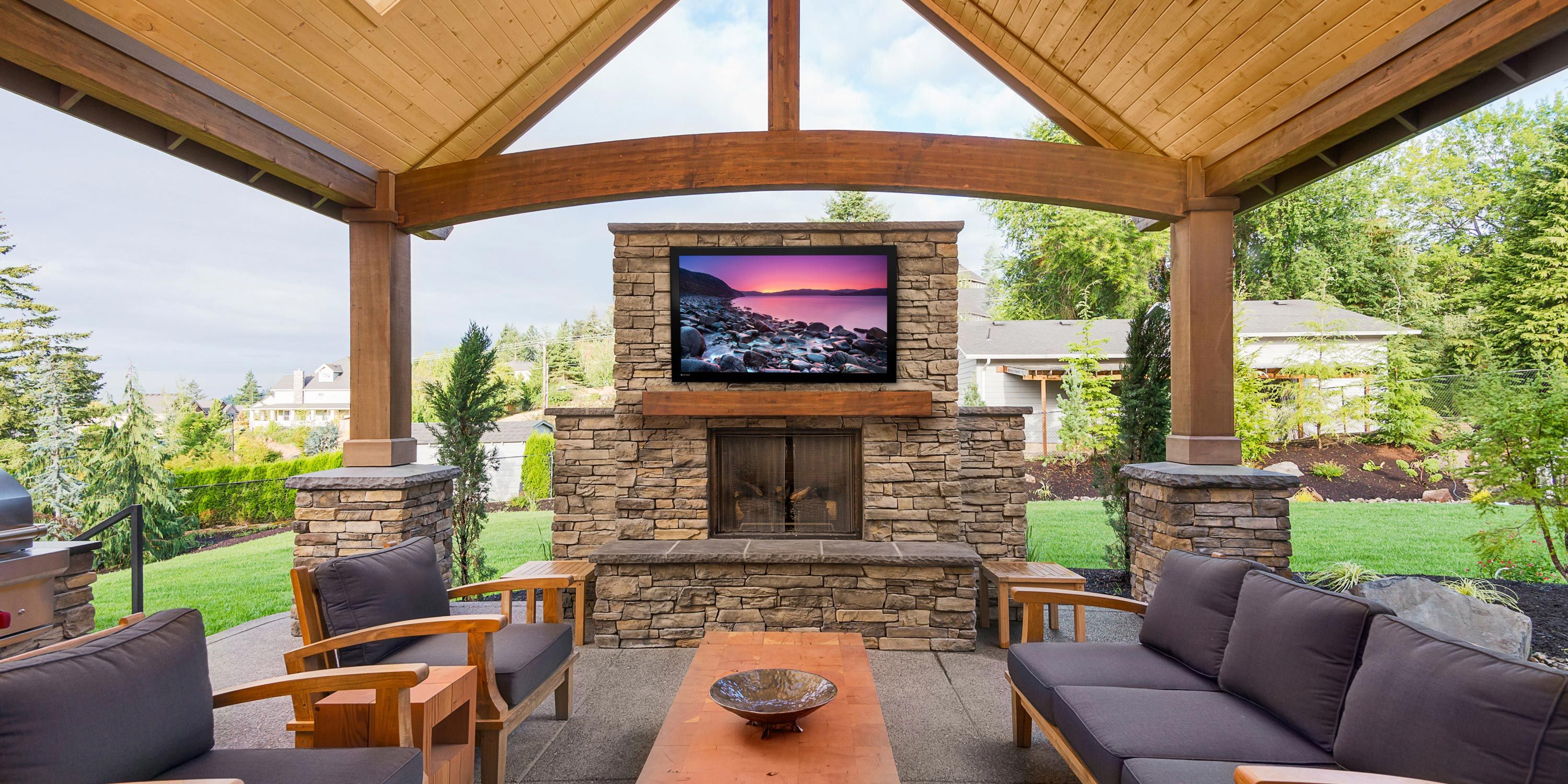 Inviting patio with a wooden roof, stone fireplace, and comfortable seating, overlooking a lush backyard.